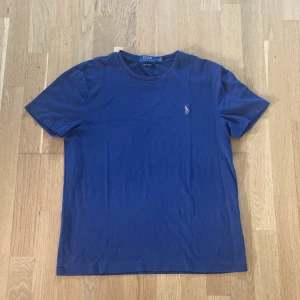 Marinblå t-shirt Polo Ralph Lauren M - Snygg marinblå t-shirt från Polo Ralph Lauren i bomull. Klassisk modell med korta ärmar, rund hals och broderad logga på bröstet. Custom slim fit för en modern och smalare passform. Perfekt till jeans eller shorts.