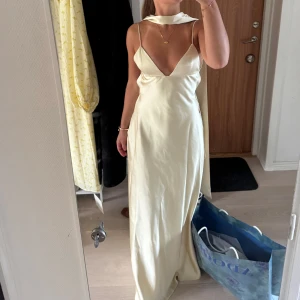 Ljus långklänning i satin med öppen rygg - Säljer min superfina klänning. Den är endast använd en gång. Ljusgul/champangig långklänning i satin med  v-ringning, tunna axelband, scarf och öppen rygg med knyt. 
