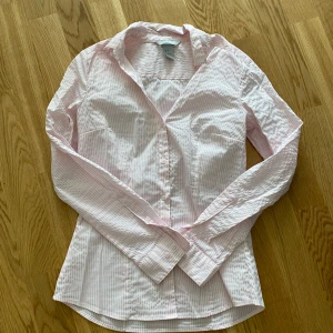 Rosa- och vitrandig skjorta från H&M - Snygg rosa- och vitrandig skjorta från H&M i storlek 36. Skjortan har klassisk krage, långa ärmar och knäppning framtill. Perfekt för en fräsch och stilren look. Tillverkad i mjuk bomull som känns skön mot huden.