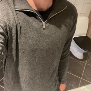 Grå half zip tröja Jack & Jones M - Mörkgrå långärmad tröja från Jack & Jones i storlek M. Tröjan har en snygg half zip-dragkedja vid halsen och är gjord i mjukt material som känns skönt mot huden. Perfekt för lager-på-lager och chill vardagsstil.