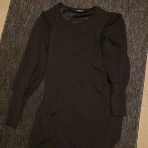 Svart långärmad klänning SHEIN - En svart, figurnära klänning från SHEIN med långa ärmar och rund halsringning. Klänningen har en enkel och stilren design som passar perfekt till olika tillfällen. Materialet känns mjukt och stretchigt för en bekväm passform.