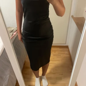 Svart tight midiklänning med knyt - Säljer en svart, tight midiklänning med knytning i ryggen och öppen rygg. Klänningen är från Gina i storlek 34💗 Bara använd en gång men har små rivningar(skriv om du vill ha bilder)