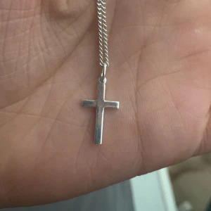Silverhalsband med kors - Stilrent halsband i silver med ett klassiskt kors som hänge. Kedjan är tunn och smidig, perfekt för dig som gillar minimalistiska smycken. Passar både till vardagslooken och när du vill addera en enkel detalj till din outfit.
