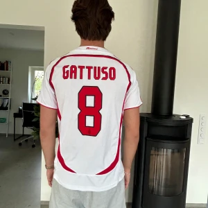 AC Milan Gattuso 8 Champions League tröja - Säljer en AC Milan bortatröja från Champions League-finalen 2007 med Gattuso och nummer 8 på ryggen. Tröjan är vit med röda och svarta detaljer, Adidas-logga, klubbmärke och Bwin som sponsor. Tillverkad i lätt och ventilerande material, perfekt för fotbollsfans.