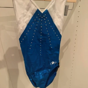 Blå och vit gymnastikdräkt  - Snygg blå och vit gymnastikdräkt  med glittrande material och silvriga detaljer. Framsidan är dekorerad med små stenar som ger extra bling. Perfekt för träning eller tävling inom gymnastik. Nästan aldrig använd.  Storlek XS