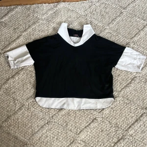 Svartvit pikétröja från Margo Collection - Cool svartvit pikétröja från Margo Collection med kontrasterande vita detaljer på krage, ärmslut och nederkant. Tröjan har v-ringad krage och trekvartsärmar, loose fit och är perfekt för en chill och trendig look.