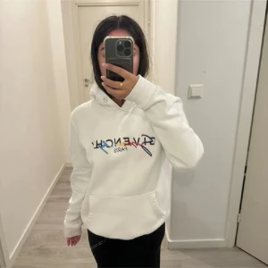 Vit Givenchy hoodie med broderad logga - Säljer en vit hoodie från Givenchy med broderad logga i flera färger på bröstet. Hoodien har huva, magficka och långa ärmar. Finns en fläck som syns på sista bilden
