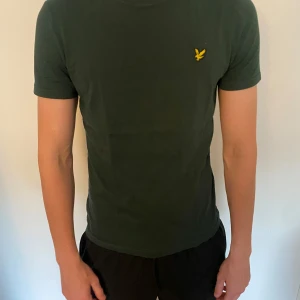 Mörkgrön t-shirt från Lyle & Scott - Snygg mörkgrön t-shirt från Lyle & Scott med klassisk gul logga på bröstet. Modellen är slim och har korta ärmar. Mycket bra skick! Och används ett fåtal gånger 