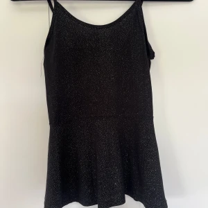 Svart glittrig festtopp med smala axelband - Supersöt svart och glittrig topp  med smala axelband detaljer över. Toppen är lite utsvängd där nere! Strl 146-152 men sitter som en. XS/XXS