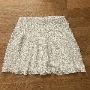 Vit kortkjol från Gina Tricot XS - Supersöt vit kortkjol från Gina Tricot i storlek XS. Kjolen har en bubblig, strukturerad yta och är lätt utsvängd för en feminin look, har även en strukturerad söm som ger effekten att kjolen ser smalare ut. Perfekt för varma dagar och enkel att matcha med crop tops eller oversized tröjor.