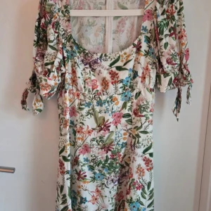 Blommig kortklänning från & Other Stories - Superfin kortklänning från & Other Stories med färgglatt blommönster på vit botten. Klänningen har puffiga korta ärmar med knyt och en rundad urringning. Perfekt för sommarens alla tillfällen och ger en romantisk vibe. 