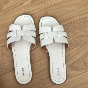 Vita sandaler från Nelly - Stilrena vita sandaler från Nelly med fyrkantig tå och breda remmar i skinnimitation. Tofflorna är för stora för mig och tänker att någon annan kan få bättre användning av dom
