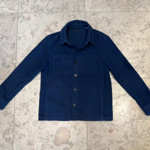 Donce De La Sense Overshirt  - Overshirt i mörkblått från Donce De La Sense, med två bröstfickor och knäppning framtill. Overshirten är i mjukt material och har klassisk krage samt långa ärmar. Perfekt för lager-på-lager och enkel att styla till olika outfits. Jag skulle säga att den passar mellan 170-180. Overshirten är använd, men är fortfarande i toppskick. Köpt ny för 1499kr. Mitt pris 799kr