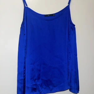 Topp - En kornblå linnetopp med tunna axelband och glansig satinfinish. Toppen har en enkel, rak passform och är perfekt för dig som gillar färgstarka och stilrena plagg. Snygg att styla med både jeans och kjol för en trendig look.