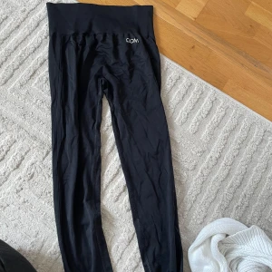 Svarta leggings från Drop of Mindfulness - Svarta, högmidjade leggings från Drop of Mindfulness med bred ribbad midja och diskret logga framtill. Tillverkade i stretchigt material av 96% polyamid och 4% elastan, perfekta för träning eller chill. Snygg och tight passform som sitter på plats hela dagen.