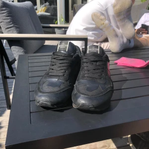 Svarta Valentino Rockrunner sneakers - Säljer ett par svarta Valentino Rockrunner sneakers med coola nitar på hälen och snygga paneler i skinn och mocka. Skorna har snörning och en chunky sula som ger en edgy vibe. Perfekta för dig som vill sticka ut med en lyxig streetstyle-look.