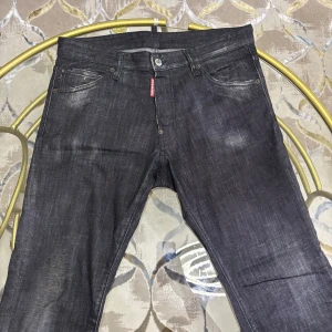 Svarta jeans från Dsquared2 - Snygga svarta jeans från Dsquared2 med diskret slitning och klassisk femficksmodell. Jeansen har en mörk tvätt, silverfärgade knappar och Dsquared2-logga på röd etikett vid gylfen. Perfekta för dig som gillar en stilren men edgy look.