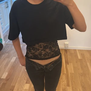 Svart croppad topp med spets från Zara - Säljer en svart croppad topp från Zara med korta ärmar och rund hals. Under delen är i genomskinlig spets med blommigt mönster och smala axelband. Perfekt för dig som vill ha en edgy och trendig look med lager-på-lager känsla. Storleken är S men passar perfekt för Xs.