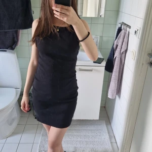 Svart ribbad ärmlös kortklänning - En svart, tight och ribbad kortklänning med ärmlös design. Klänningen har en enkel och stilren look med rund halsringning och kroppsnära passform. Perfekt för dig som gillar minimalistisk stil och vill ha något som är både bekvämt och snyggt.