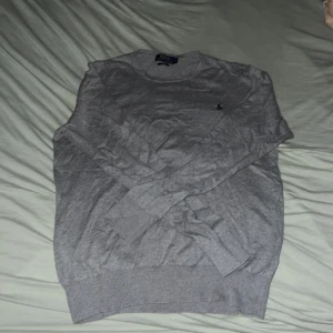 Grå slim fit tröja Polo Ralph Lauren - Snygg grå långärmad tröja från Polo Ralph Lauren i slim fit-modell. Klassisk design med rund hals och diskret broderad logga på bröstet. Perfekt för dig som gillar stilrena och enkla plagg. Tillverkad i mjuk bomull för skön känsla.