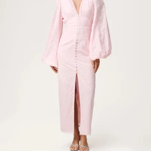 Ljusrosa långklänning med puffärmar - Superfin ljusrosa långklänning från Adoore med broderade blommor, djup v-ringning och stora puffärmar. Klänningen har knappar framtill och en slits nedtill. Perfekt för dig som vill sticka ut med en romantisk och trendig look.