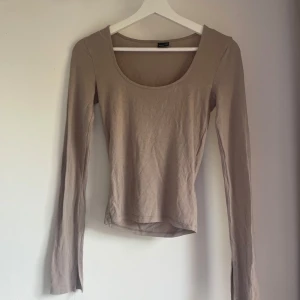Beige långärmad topp från Gina Tricot - Superenkel och snygg beige långärmad topp från Gina Tricot i mjuk bomull. Modellen har rundad, djup urringning och slits vid ärmsluten för en extra detalj. Perfekt att styla med jeans eller kjol för en clean look.