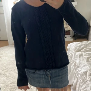 Mörkblå stickad tröja från Pelle P - Mörkblå stickad tröja från Pelle P med snyggt flätmönster framtill och rund hals. Tröjan har lång ärm och en broderad logga på ena ärmen. Perfekt för dig som gillar klassisk och stilren look.
