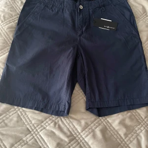 Mörkblå Sail Racing shorts - Snygga mörkblå shorts från Sail Racing med klassisk passform och raka ben. Shortsen har sidofickor, bälteshällor och en bakficka med Sail Racing-logga. Tillverkade i bomull, perfekta för sommardagar. Enkla att matcha och riktigt stilrena.