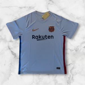 Blå FC Barcelona Nike fotbollströja - Snygg ljusblå FC Barcelona matchtröja från Nike med klubbmärke och Rakuten-tryck på bröstet. Tröjan har korta ärmar, V-ringning och är tillverkad i ett lätt, ventilerande material. Sidorna har blå och röda detaljer och Unicef-logga finns på ryggen.