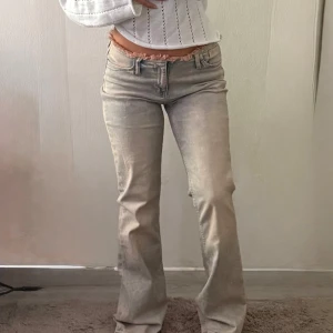 Lågmidjade bootcut jeans från H&M Divided - Snygga lågmidjade bootcut jeans från H&M Divided i ljusblå tvätt. Jeansen har rosa fransad midja, stängs med dragkedja och en genomskinlig liten knapp. Aldrig använda, endast för bilden. 