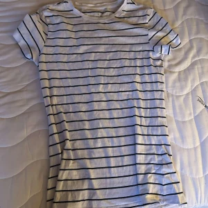 Vit randig t-shirt från Primark - Vit t-shirt från Primark med svarta horisontella ränder. Klassisk rund halsringning och korta ärmar. Tillverkad i stretchig bomull som sitter skönt och följsamt. Perfekt för en chill och stilren look.