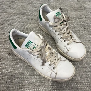 Adidas Stan Smith vita sneakers - Klassiska Adidas Stan Smith sneakers i vitt med gröna detaljer. Skorna är väll använda men tänkte att jag testar lägga ut de för en billig peng för de som inte har så bra ekonomiskt ställt ☺️(köper man nya skosnören och rengör dom noggrannare tror jag dom kan bli jätte snygga) 