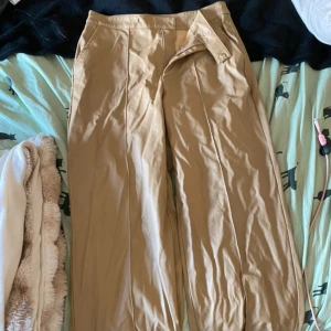 Beiga vida byxor - Snygga beiga byxor med vida ben och hög midja. Byxorna har pressveck framtill och sidfickor, perfekta för en clean och stilren look. Tillverkade i ett mjukt bomullsmaterial som känns skönt mot huden.
