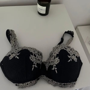 Mörkblå spets-bh med  broderi - Snygg mörkblå bh med broderade spetsdetaljer på kupor och axelband. Väl använd men i ett bra skick!