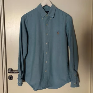 Ralph lauren Skjorta - En blå skjorta från Ralph lauren i storleken M och som är normal i storleken. Skjortan har ett mycket bra skick fast ett litet hål vid ena armen. Vid funderingar är det bara att höra av sig!