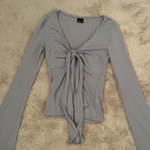 Ljusblå långärmad topp med knyt - Trendig ljusblå topp med långa ärmar och snygg knytning framtill. Djup v-ringning och figurnära passform. Perfekt att styla med jeans eller kjol för en cool look.