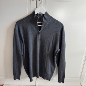 Grå halvzip tröja från Mango man - Säljer en stilren grå långärmad tröja från Mango med halv dragkedja och hög krage. Perfekt för lager-på-lager och passar till många olika outfits. Mjuk och bekväm, tillverkad i bomullsmix.