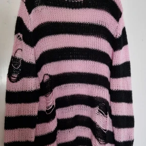 Randig Killstar tröja - Säljer en oversized stickad tröja från Killstar i rosa och svart med breda ränder. Tröjan har lång ärm och flera slitna detaljer för en edgy look. Perfekt för dig som gillar alternativ stil! Köptes för 550 kr. Köparen står för frakt!