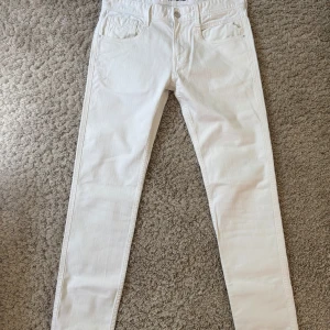 Vita Replay Anbass jeans 30/32 - Säljer ett par vita Replay Anbass jeans med klassisk femficksdesign och raka ben. Byxorna har diskreta detaljer och logotyp på bakfickan. Perfekta för dig som vill ha ett stilrent och fräscht plagg i garderoben.