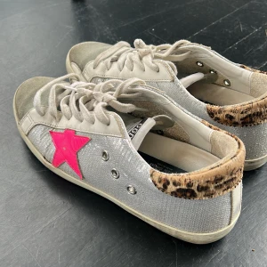 Silverfärgade sneakers från Golden Goose med leoparddetalj - Säljer ett par snygga sneakers från Golden Goose i glittrig silver, rosa stjärna på sidan och leopardmönstrad häl. Skorna har vita snören och är perfekta för sommaren🫶