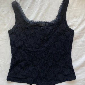 Svart goth korsetttop  - Säljer ett svart linne från Fransa med vacker spets och liten rosett framtill. Linnet har breda axelband och är figurnär i modellen. Gott skick 