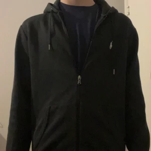 Svart hoodie Polo Ralph Lauren - Svart hoodie med dragkedja från Polo Ralph Lauren. Bra skick men tyvärr en fläck av målarfärg på högerarmen, därav priset. Storlek S och modellen på bilden är 183cm. Hör av er vid frågor eller funderingar! 