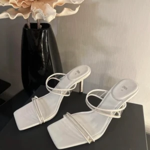 Vita sandaler/klackskor från Zara - Säljer ett par stilrena vita sandaler från Zara med smala remmar och fyrkantig tå. Skorna har en låg klack och öppen design, perfekta för varma dagar. Snygga att matcha till både jeans och klänning.