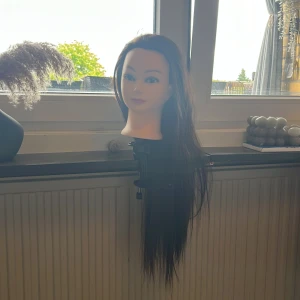 Träningshuvud med långt mörkbrunt hår - Träningshuvud med extra långt, rakt och mörkbrunt hår. Perfekt för övning av frisyrer, flätor och styling. Huvudet har naturlig ansiktsform och markerade ögonbryn samt läppar. Lätt att borsta ut och håller stylingen. Har inte testat att platta/locka det så den är helt frisk! 