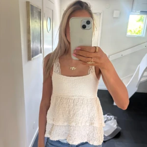 Vit volangig linnetopp - Säljer en söt vit linnetopp med volanger och smala axelband. Toppen har en lätt strukturerad yta och är perfekt för varma dagar. Passar snyggt till jeans eller kjol.