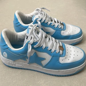 BAPE STA sneakers i blått och vitt - Säljer ett par BAPE STA sneakers i blankt blått och vitt med klassisk stjärndesign på sidan. Skorna har vita snören, rund tå och platt sula. Perfekta för dig som vill sticka ut med streetwear-stil.