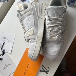 Vita Louis Vuitton trainers  - Säljer ett par vita Louis Vuitton sneakers med klassiskt LV-monogram på ovandelen och sidan. Skorna har snörning, rund tå och platt sula. Perfekta för dig som vill ha en lyxig och stilren look. Öppen för byten, säljes billigt då utav slitage 