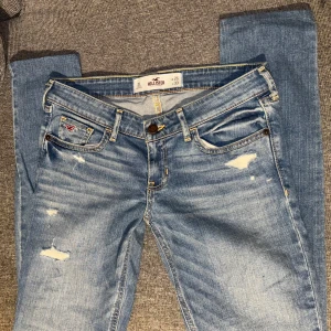 Ljusblå slitna jeans från Hollister - Jätte lågmidjade jeans perfekta för att göra om till ett par jeansshorts, jeanskjol eller att sy bootcut! Små i storleken så skulle säga dem sitter som stl 25💓