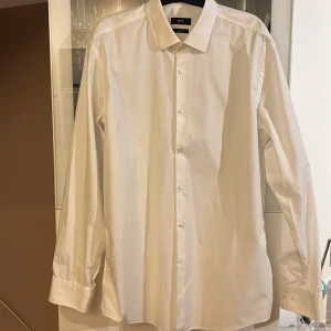 Vit skjorta från BOSS - Klassisk vit skjorta från BOSS med slim fit-passform. Skjortan har långa ärmar, knappar framtill och en stilren krage. Perfekt för dig som vill ha en enkel och snygg skjorta till garderoben. Pris går att diskuteras,nästan nyskick