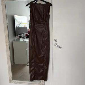 Brun långklänning i skinnimitation - Säljer en brun långklänning i skinnimitation med ärmlös design och slits bak. Klänningen har en figurnära passform och en stilren look som passar perfekt till speciella tillfällen. Från shein. Använd två tre gånger